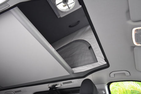 This RV rental interior shows a pop-top roof extended, revealing an overhead bed with a fan. Clear and spacious.