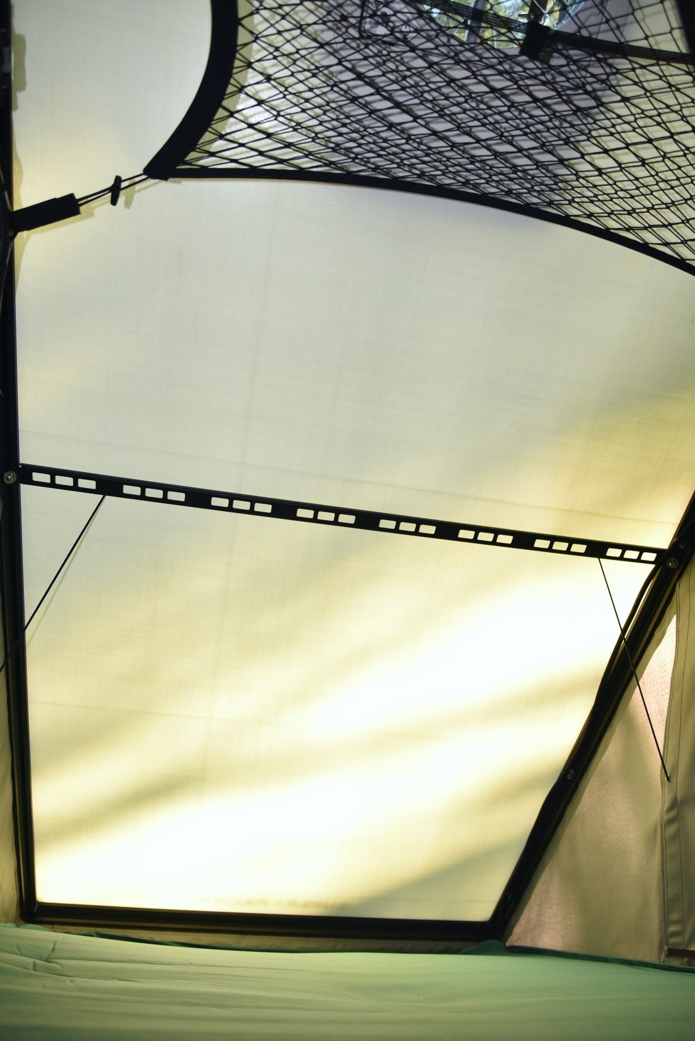Interior of an RV rental pop-up tent, showing overhead mesh, bright translucent fabric walls, and a green sleeping pad. — photo 4