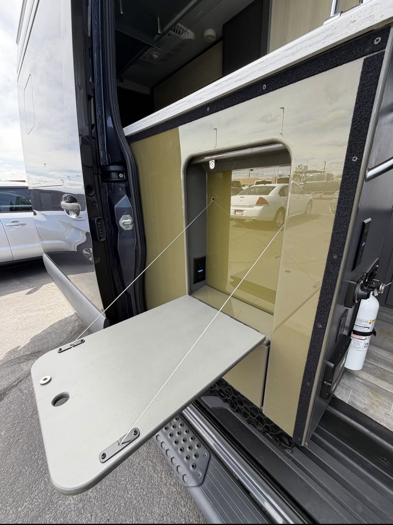 RV rental with side entry showing a fold-down table, USB/power port, and fire extinguisher for outdoor convenience.