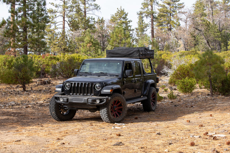 Black Jeep Gladiator with rooftop tent in a forest, perfect for your next rv rental adventure. — photo 1