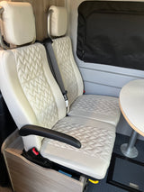 Comfortable rv rental interior with quilted white seats, table, and window blind, perfect for travel.