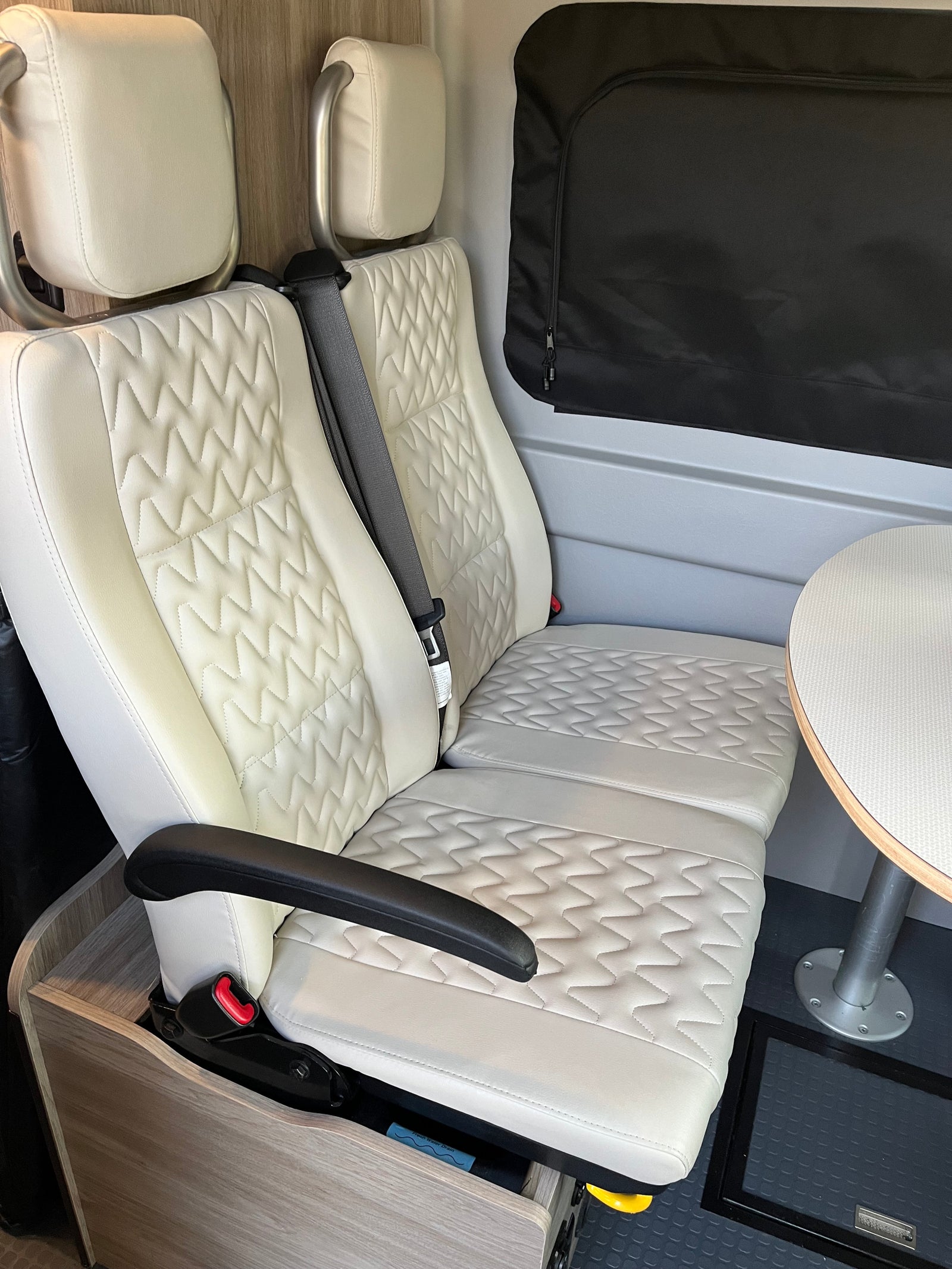 Comfortable rv rental interior with quilted white seats, table, and window blind, perfect for travel.