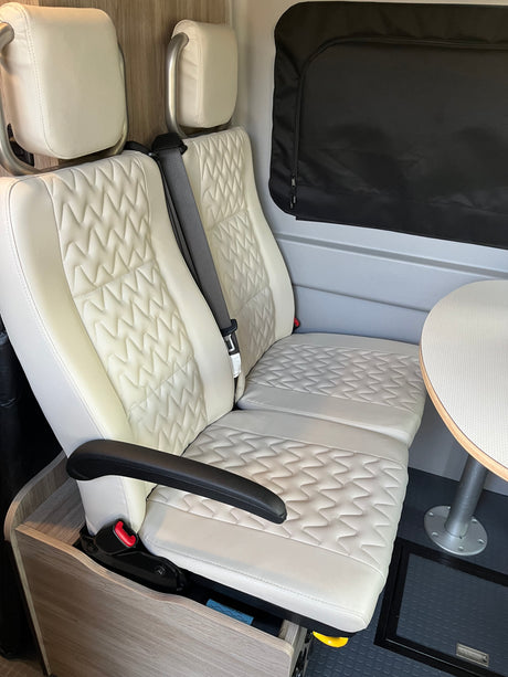 Comfortable rv rental interior with quilted white seats, table, and window blind, perfect for travel.