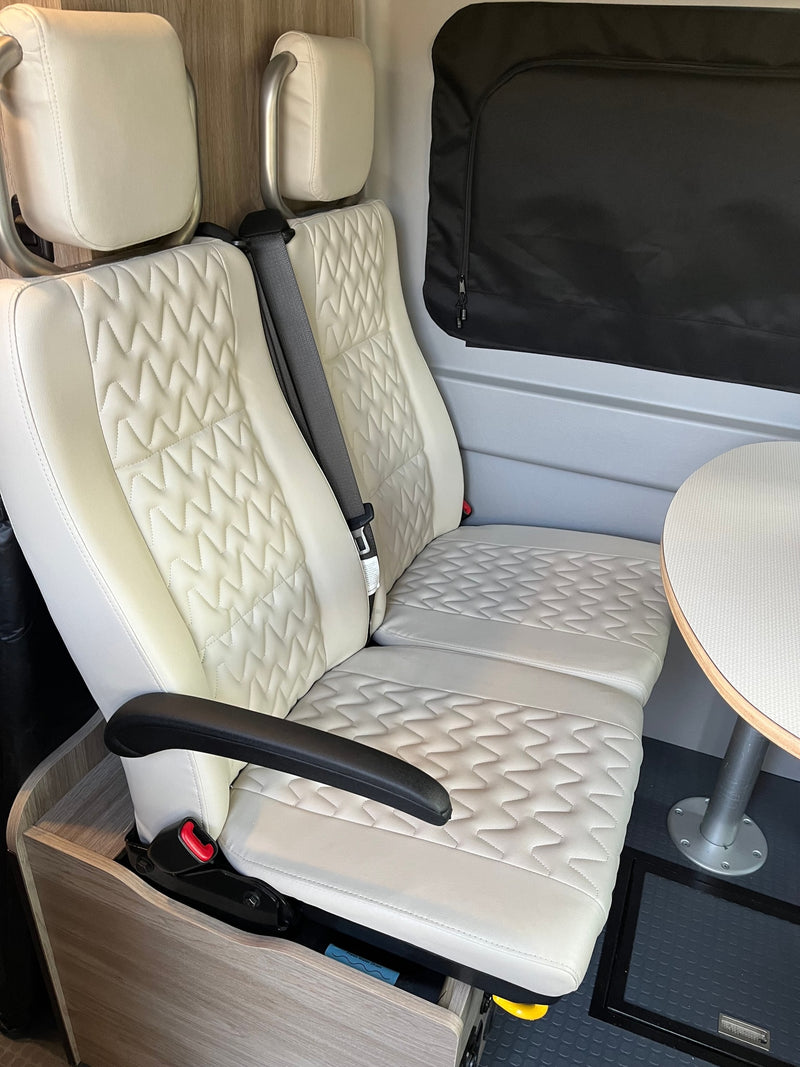 Comfortable rv rental interior with quilted white seats, table, and window blind, perfect for travel. — photo 8