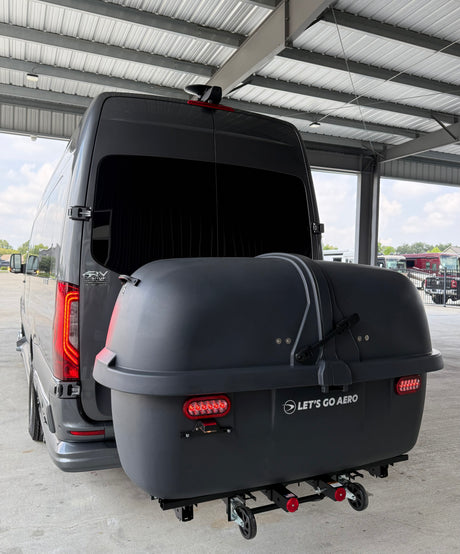 This grey RV rental van features a large "Let's Go Aero" rear cargo box, ideal for travel storage.