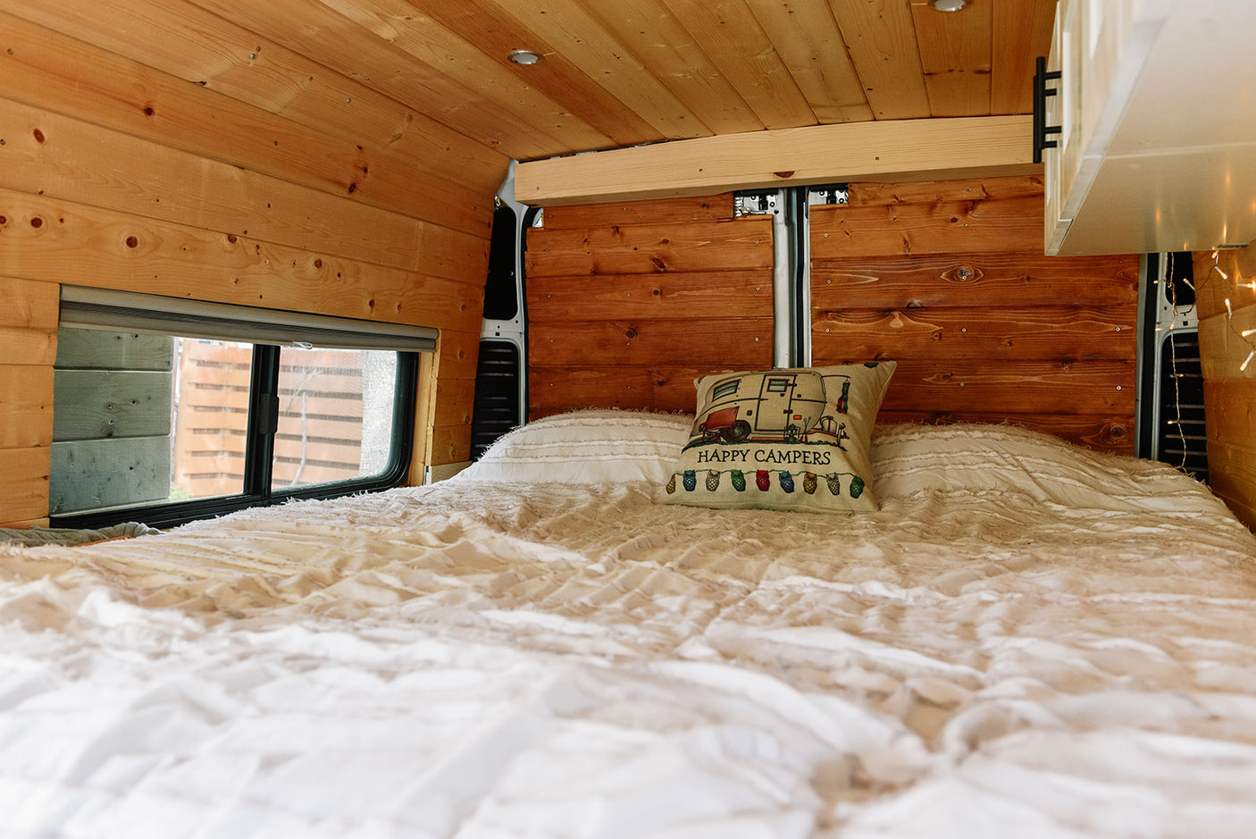 Experience a cozy RV rental: comfy bed, wood-paneled walls, and window in a modern camper van.