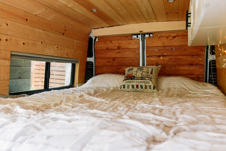 Experience a cozy RV rental: comfy bed, wood-paneled walls, and window in a modern camper van.
