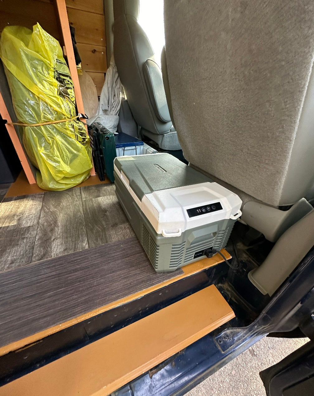 Inside a cozy RV rental: a portable refrigerator on laminate flooring, with storage and seats in view.
