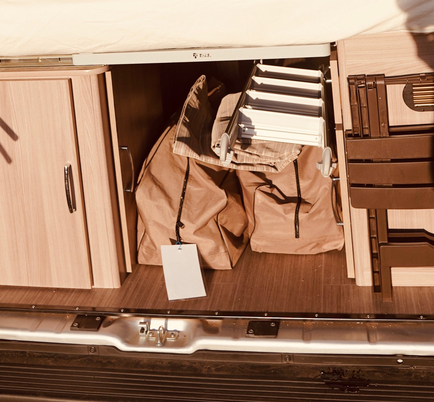 RV rental storage shows wooden cabinets, beige bags, a folded ladder, and brown camping chairs.
