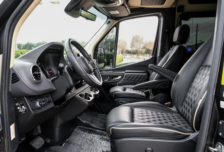 Spacious front cabin of an RV rental, featuring luxurious black leather seats with diamond stitching, steering wheel, and dashboard.