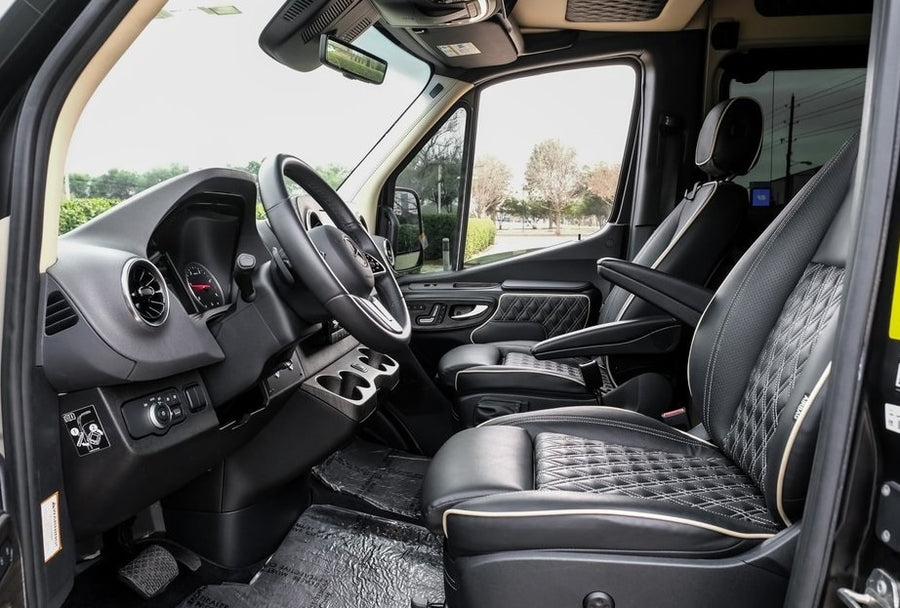 Spacious front cabin of an RV rental, featuring luxurious black leather seats with diamond stitching, steering wheel, and dashboard.