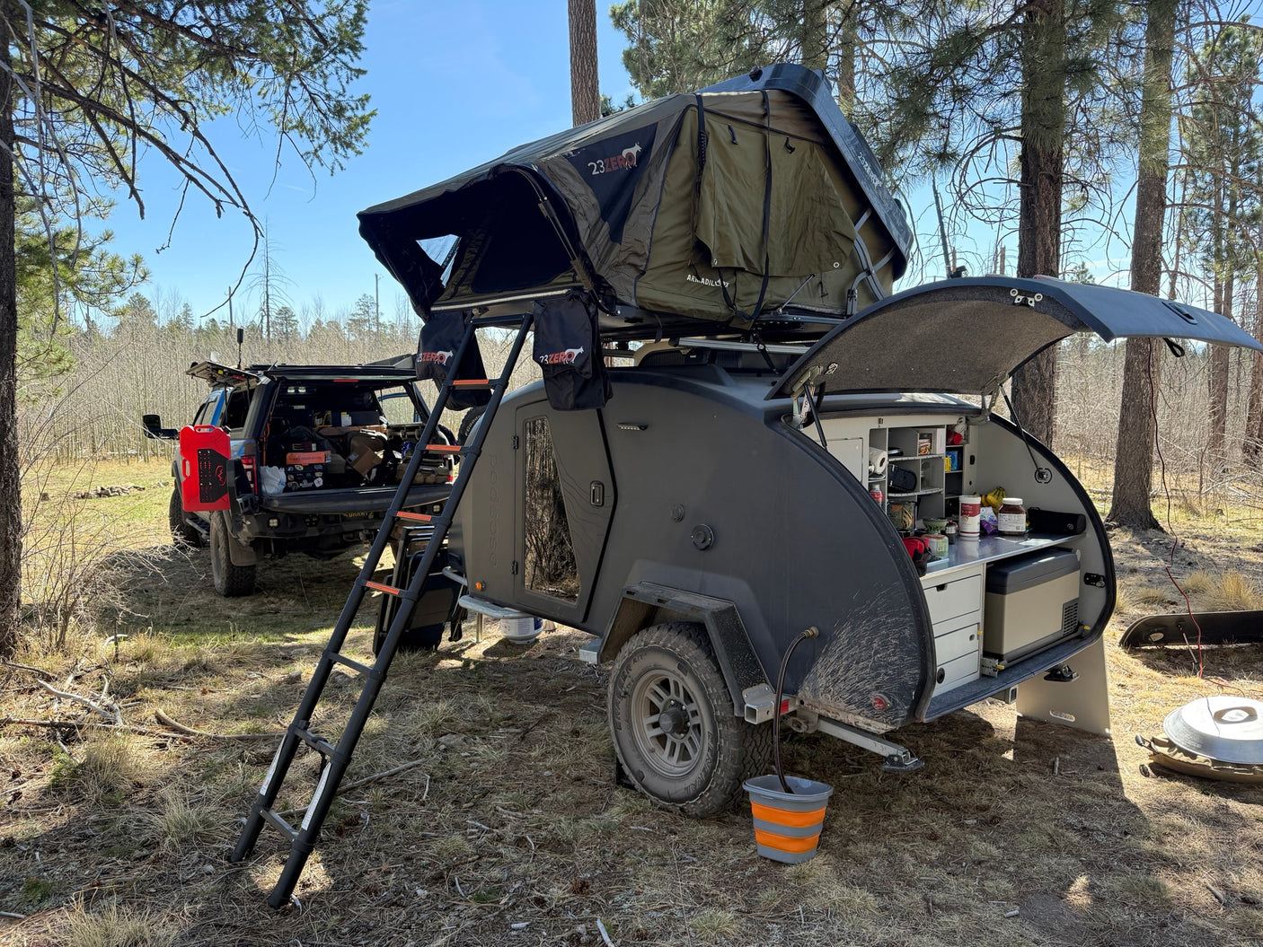Enjoy off-grid camping with this RV rental: a teardrop trailer featuring a rooftop tent, outdoor kitchen, and an overland truck.