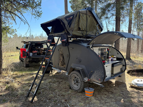 Enjoy off-grid camping with this RV rental: a teardrop trailer featuring a rooftop tent, outdoor kitchen, and an overland truck.