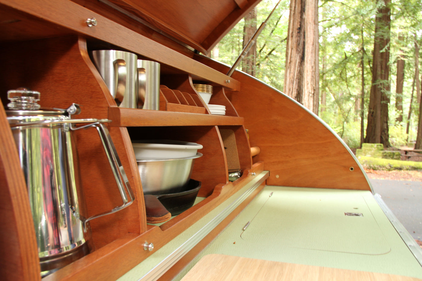 Teardrop RV rental's organized wooden galley with cookware, dishes, and an open lid revealing redwood trees. — photo 17