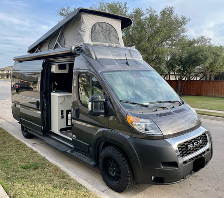 Dark gray pop-top camper van with open side door revealing a compact kitchen. Perfect for RV rental adventures!