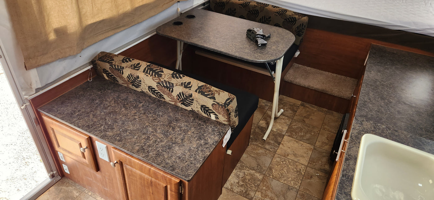Inside an RV rental: a compact dinette with a table and patterned benches, plus a kitchen counter area and tiled floor. — photo 8