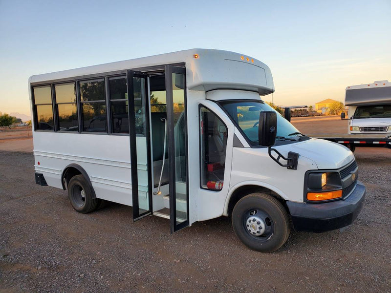 White shuttle bus with open doors on gravel, next to an RV on a trailer under a sunset sky. Potential rv rental. — photo 8