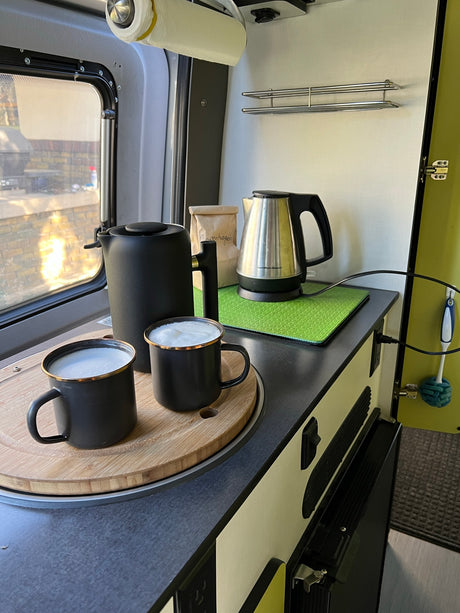 RV rental kitchen: cozy setup with frothy coffee mugs, a kettle, & French press for morning brew.