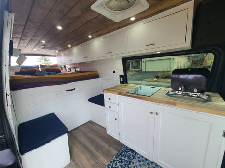 Spacious RV rental interior features modern kitchen, cozy bed, wood ceiling, and white cabinets.