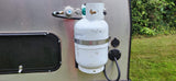 Side of an RV rental showing a propane tank with regulator and shore power inlet for outdoor living.