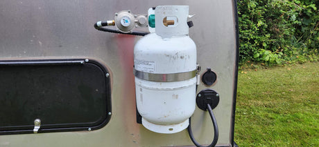 Side of an RV rental showing a propane tank with regulator and shore power inlet for outdoor living.