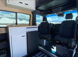 Inside a modern RV rental: a compact kitchen, comfortable front seats, and large windows revealing a beautiful snowy landscape.