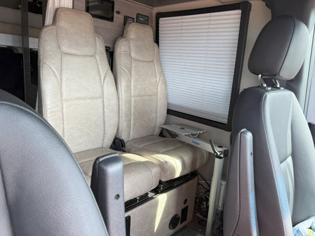 RV rental interior: beige swivel seats, window with blind, and a Lagun table mount for flexible space.