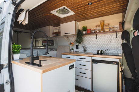 Inside this modern RV rental: A kitchen with hexagonal tile backsplash, wood counters, and a bed area in the back.