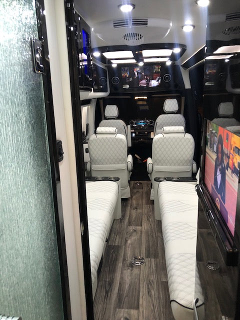 Spacious luxury RV rental interior: white quilted seats, wood flooring, and multiple screens for premium entertainment. — photo 16