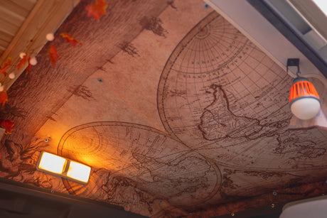 RV rental interior: The ceiling showcases a vintage world map, lit by warm strip and hanging lanterns, perfect for travel.