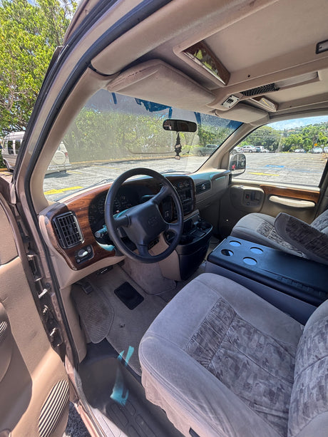 Inside a spacious RV rental van, featuring its dashboard with wood trim, steering wheel, and front seats with a large console.