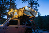 This overland RV rental setup with a lit rooftop tent on a Jeep Wrangler offers cozy camping under the twilight sky.