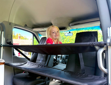 Child peeks from a fabric bunk inside an RV rental van, highlighting clever interior sleeping/storage solutions.