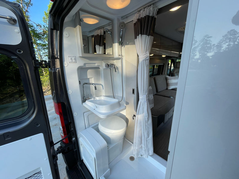 Compact RV rental wet bath inside a camper van, showing a shower, toilet, and fold-down sink with open doors. — photo 16
