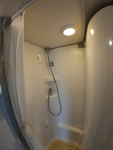 Clean, compact shower in an RV rental. Handheld showerhead, bright light, and white curtain on a track.