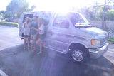 Three friends gather beside their silver **rv rental** van on a bright, sunny day, taking a break outdoors during their travels.