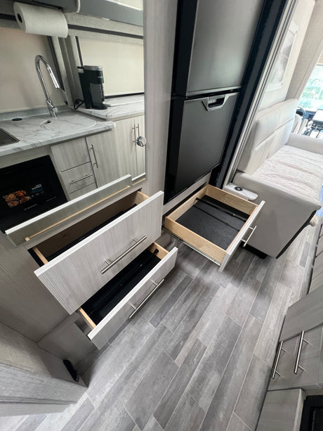 Inside a modern RV rental: open kitchen drawers, sink, microwave, fridge, and comfortable seating visible.