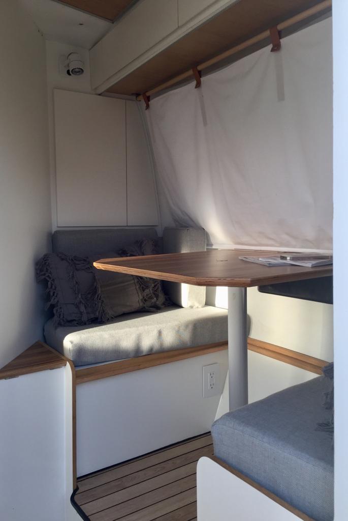 Compact RV rental interior featuring a cozy dining area with grey cushions, wooden table, and a white privacy curtain. — photo 5