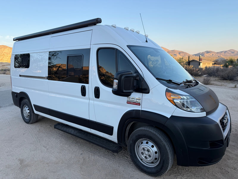 White Ram ProMaster camper van RV rental in a desert setting with mountains in the background, parked on a dirt road. — photo 1