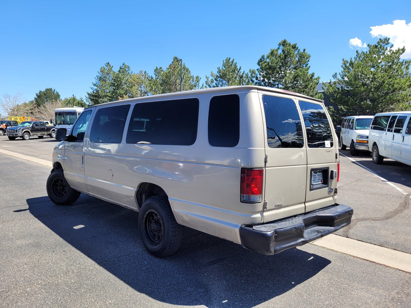 A tan Ford Econoline van, resembling an RV rental, parked on asphalt on a sunny day. Other vans nearby. — photo 3