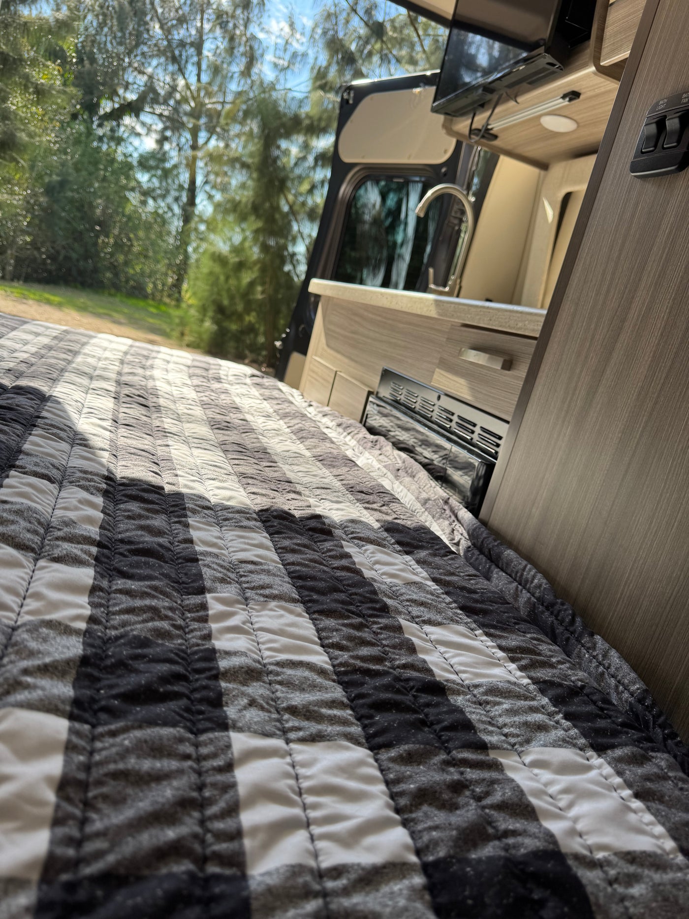 RV rental: inviting bed with black & white striped quilt, mini-kitchen, and serene nature visible through the open door. — photo 19