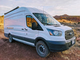 White Ford Transit camper van parked on a dirt road in a desert landscape. Perfect for an RV rental adventure!