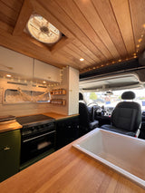Cozy RV rental interior: wooden ceiling, fan, string lights, kitchen, and front cab view.