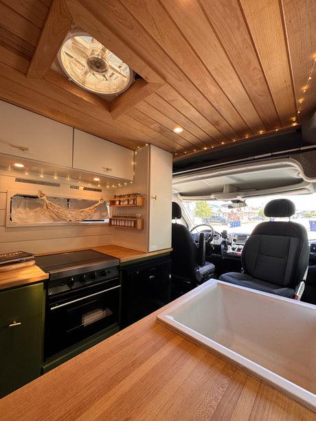 Cozy RV rental interior: wooden ceiling, fan, string lights, kitchen, and front cab view.