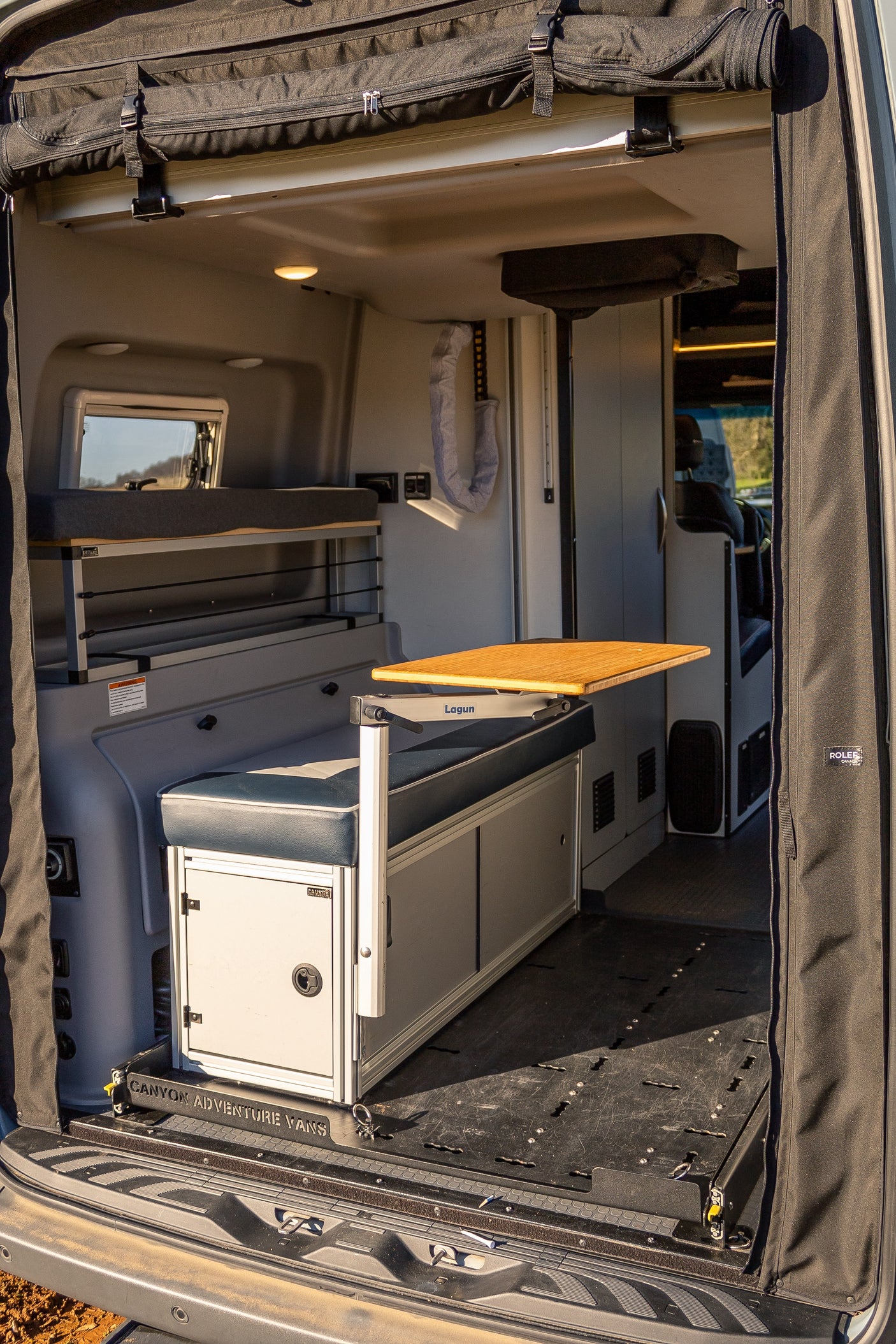 Interior view of an RV rental, showing a multi-functional space: upper bunk, bench with adjustable table, and modular floor.