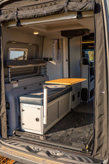 Interior view of an RV rental, showing a multi-functional space: upper bunk, bench with adjustable table, and modular floor.