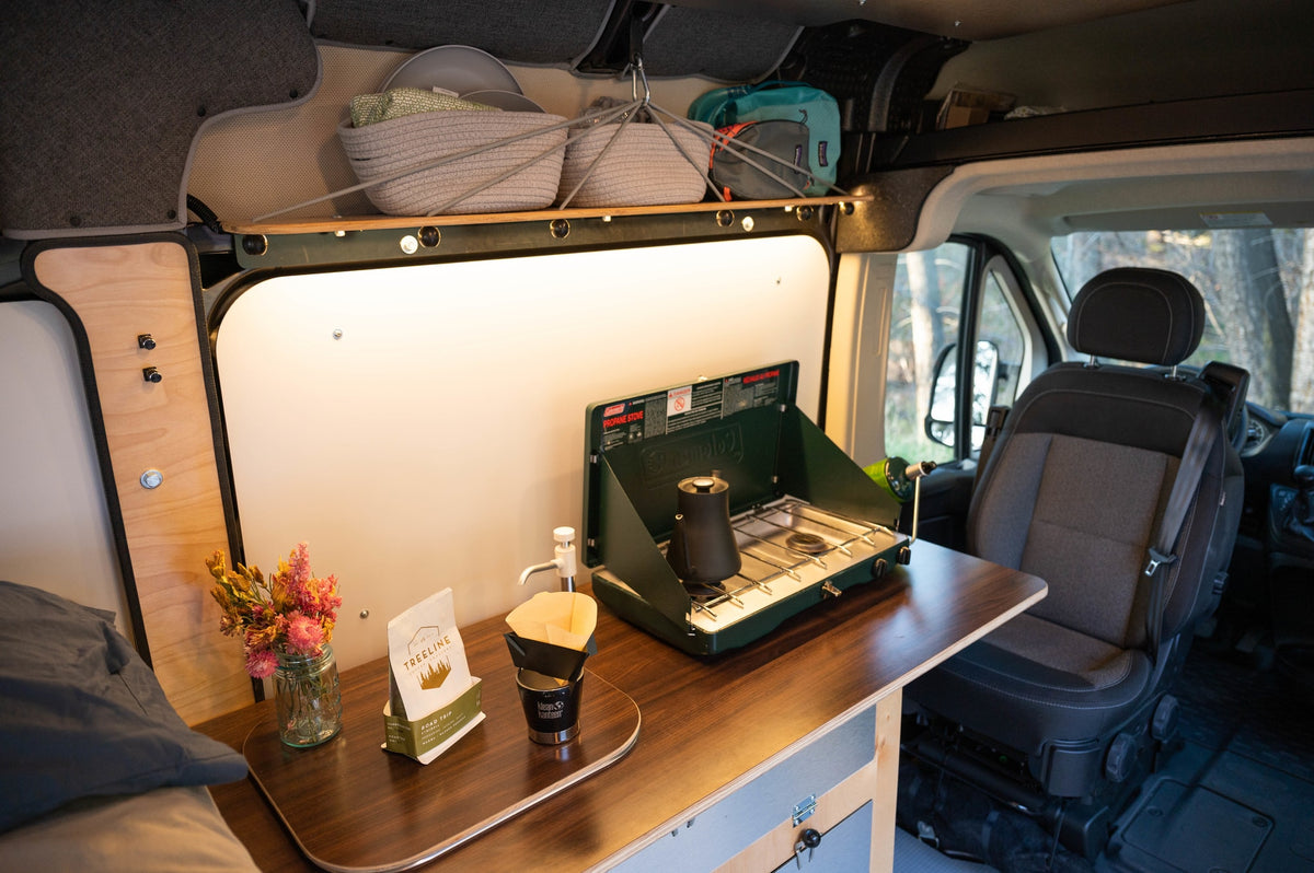 Inside a well-equipped RV rental, a kitchen area with a propane stove, coffee pour-over setup, and storage baskets for comfortable travel. — photo 17