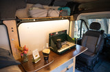 Inside a well-equipped RV rental, a kitchen area with a propane stove, coffee pour-over setup, and storage baskets for comfortable travel.