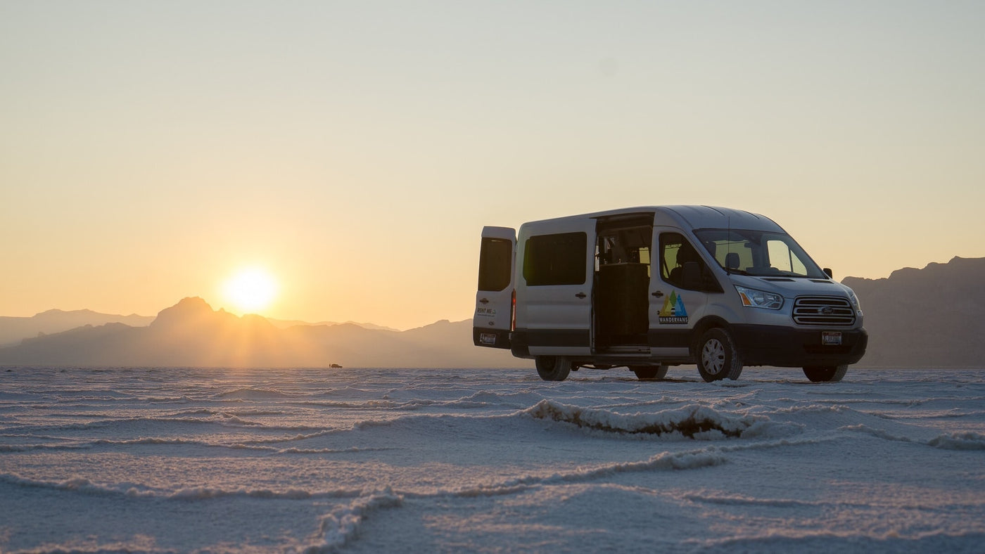 A silver Wandervans RV rental is parked on expansive white salt flats at sunset, doors open with mountains in background. — photo 16