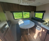 An RV interior showing a bright dinette with table, bench seating, and kitchen sink, ideal for an rv rental.